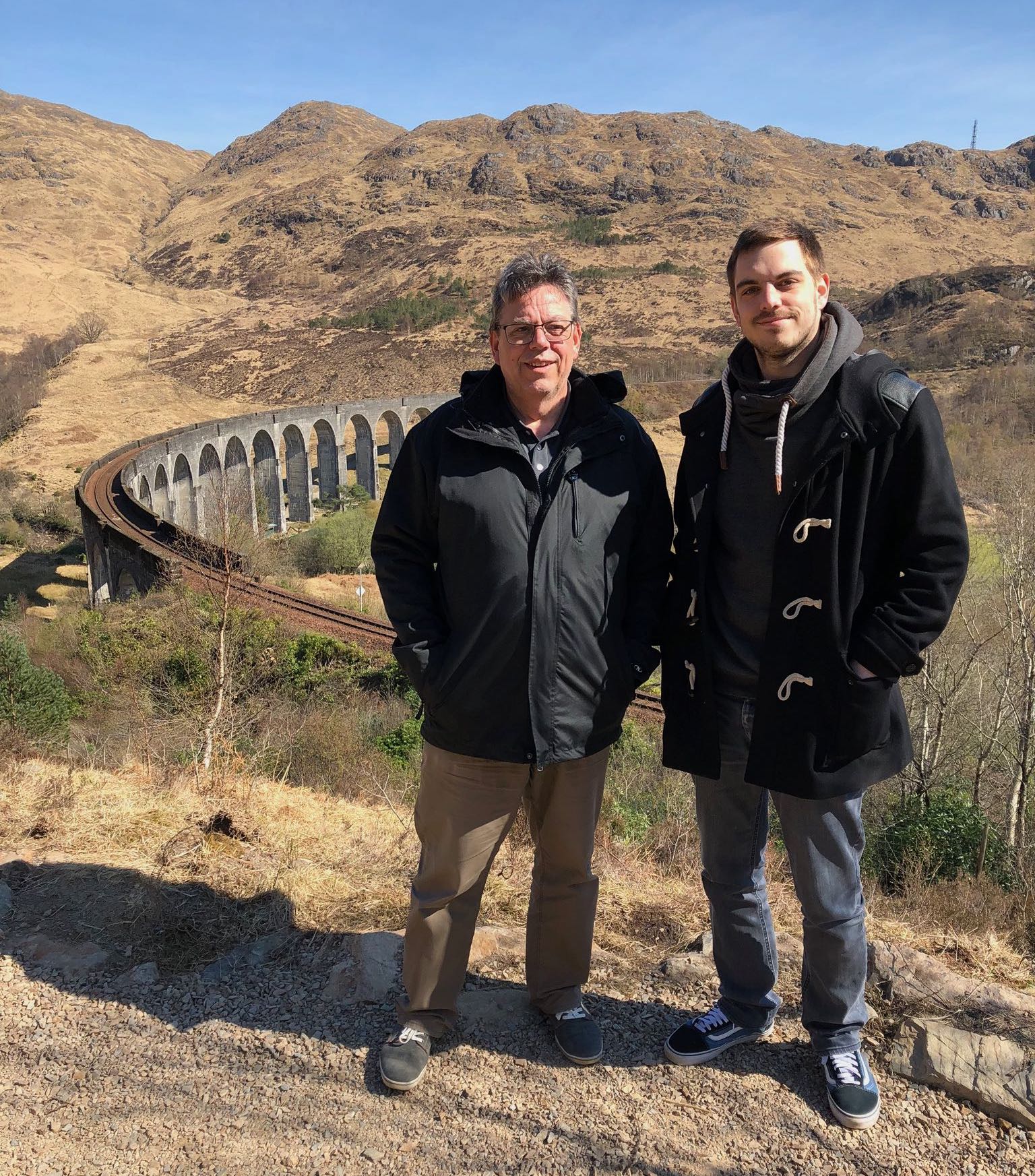 Daniel und Egon Brunner lächeln zufrieden vor dem Harry Potter Howagtrs Express Viadukt in Glenfinnan in Schottland.