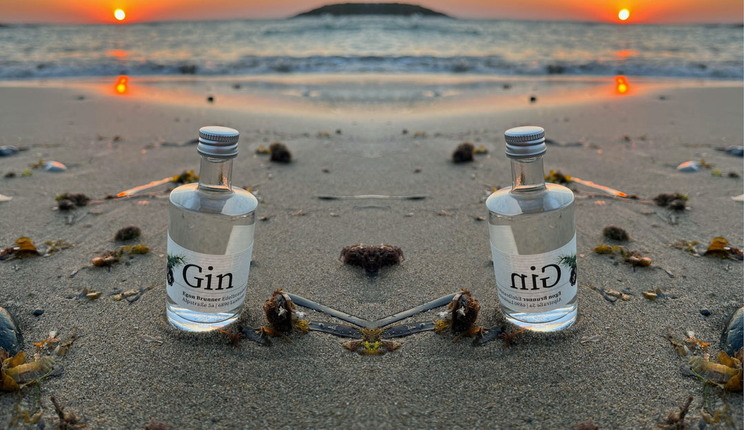 50ml Miniflasche mit Gin der Destillerie Brunner im Sand am Meer von Kreta während eines Sonnenuntergangs.