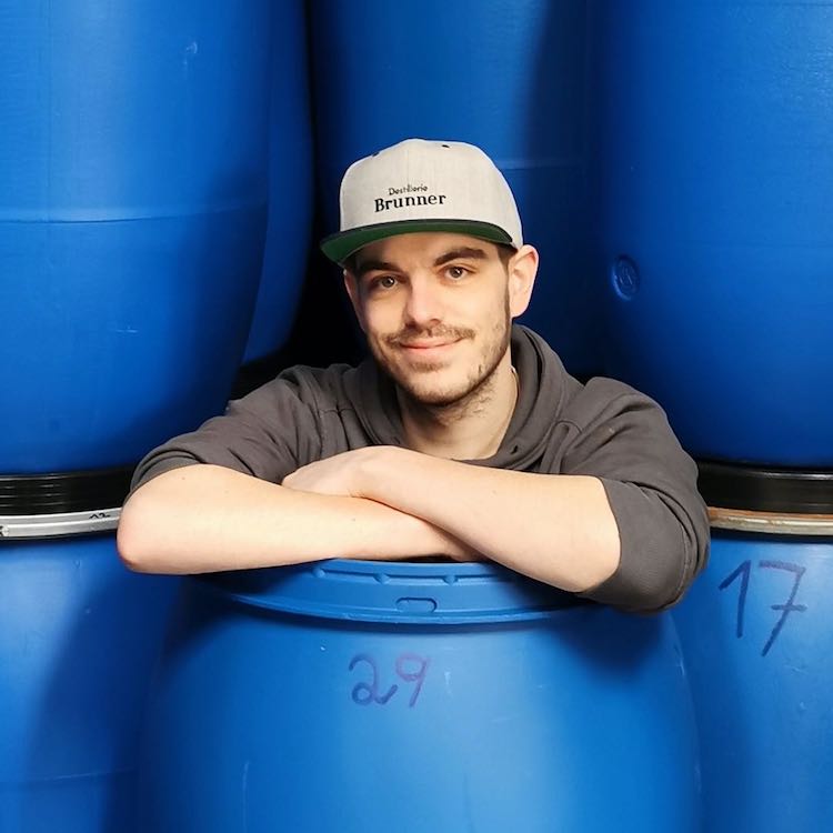 Webentwickler Daniel der Destillerie Brunner lächelnd und sitzend in einem blauen Maischefass.